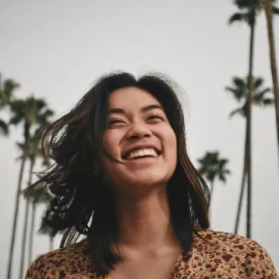 A woman stands in front of palm trees, smiling.